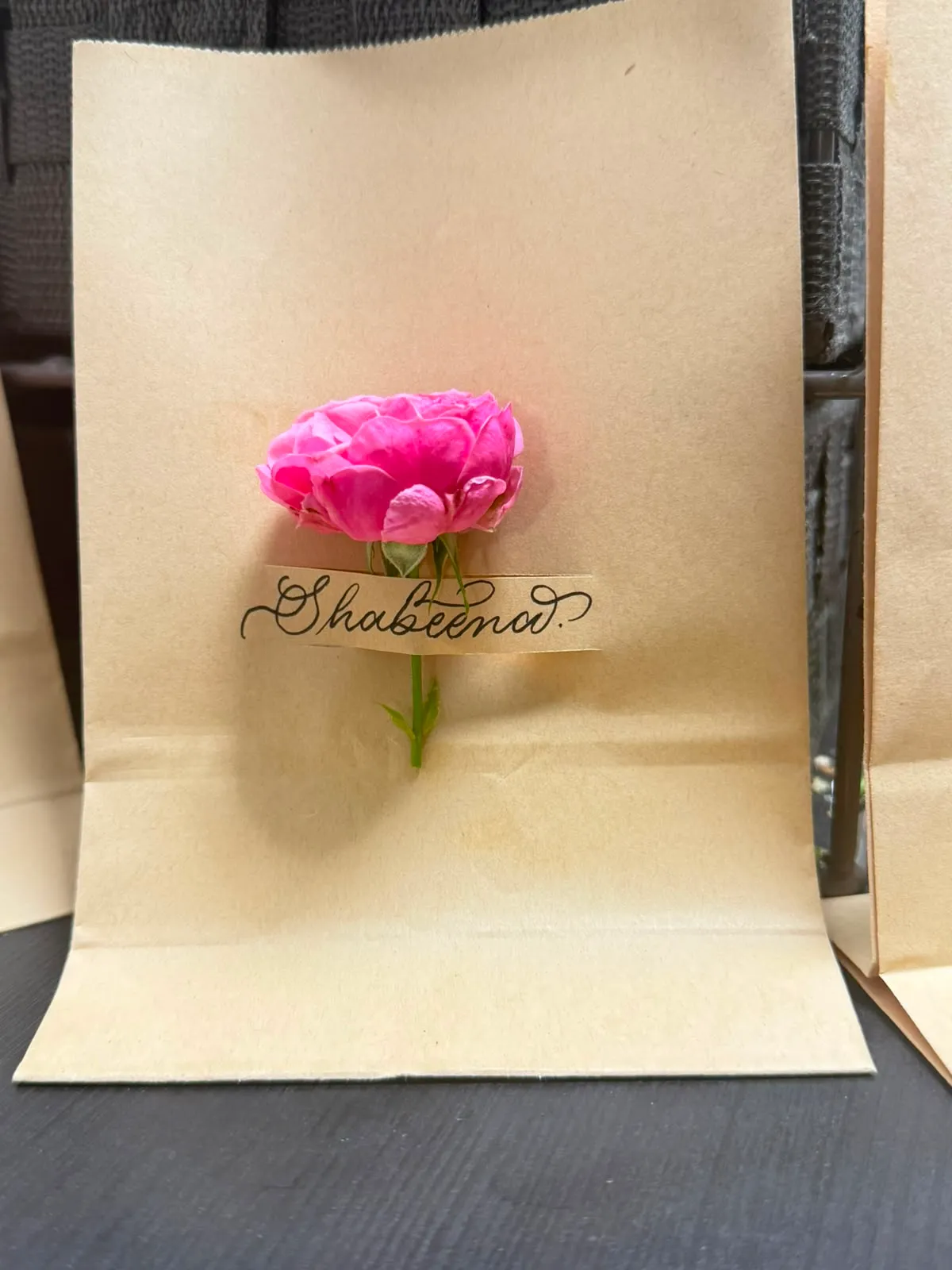 Kraft gift bag lettered “Shabeena” with a pink rose