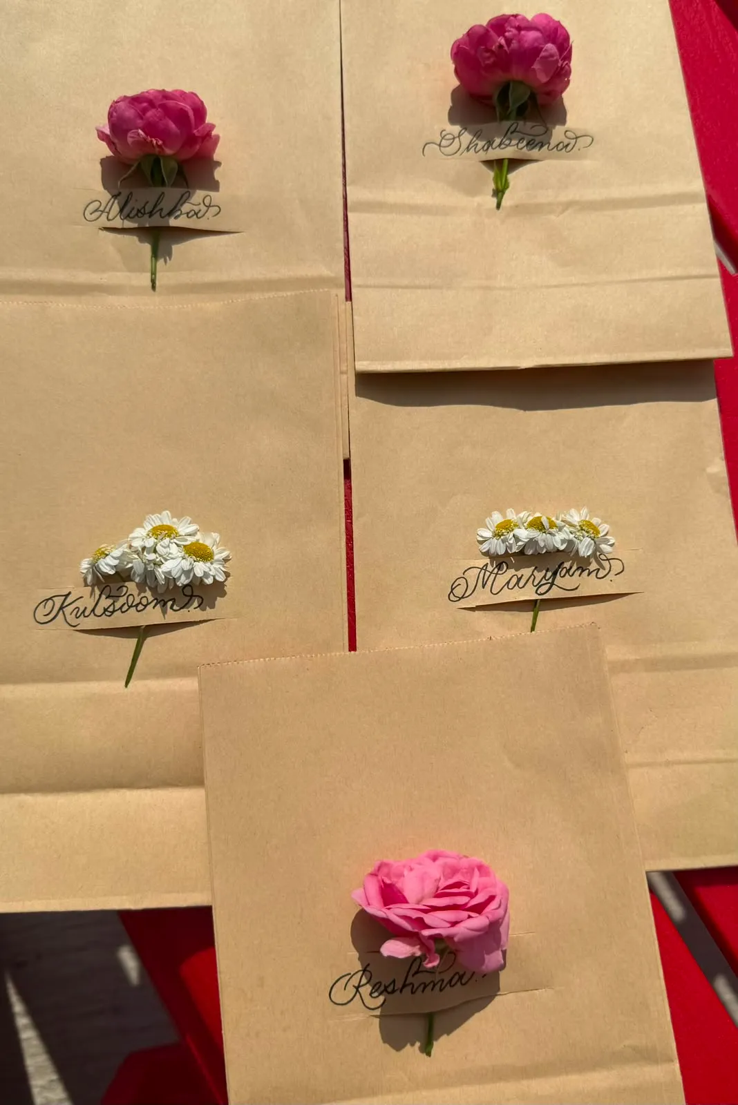 Kraft gift bags hand-lettered with names and finished with fresh roses and daisies